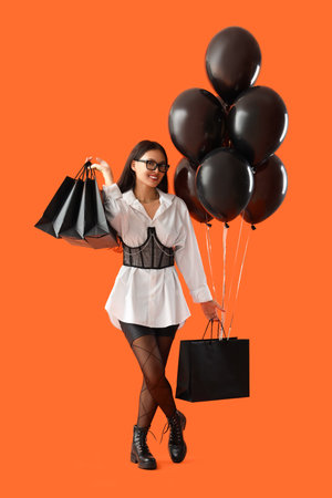 Young Asian woman with shopping bags and balloons on orange background. Black Friday saleの写真素材