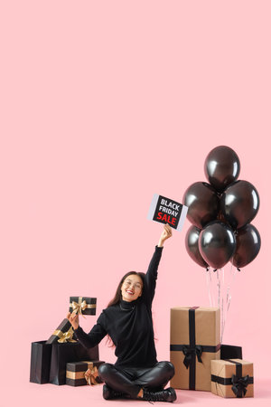 Young Asian woman with gifts and balloons on pink background. Black Friday saleの写真素材