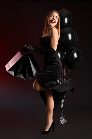 Young woman with shopping bags and balloons on dark background. Black Friday saleの写真素材