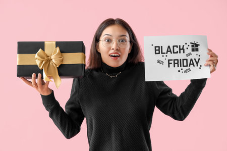 Surprised young Asian woman with gift on pink background. Black Friday saleの写真素材