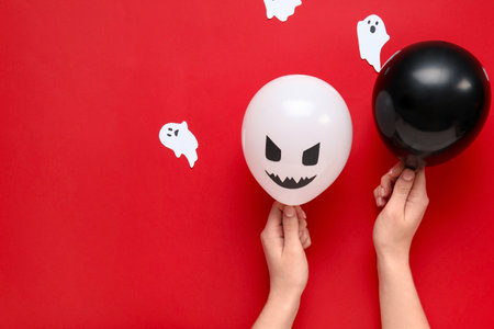 Female hands with different funny Halloween balloons and paper ghosts on red backgroundの写真素材
