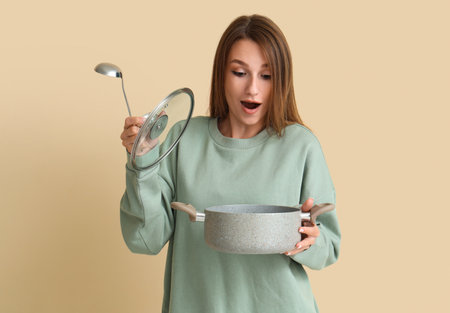 Surprised young woman with ladle and cooking pot of chicken soup on beige backgroundの写真素材