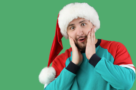 Shocked young man in Santa hat on green backgroundの写真素材