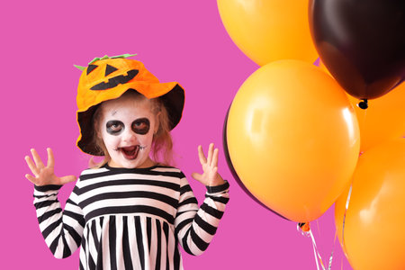 Little girl dressed for Halloween with balloons on purple backgroundの写真素材