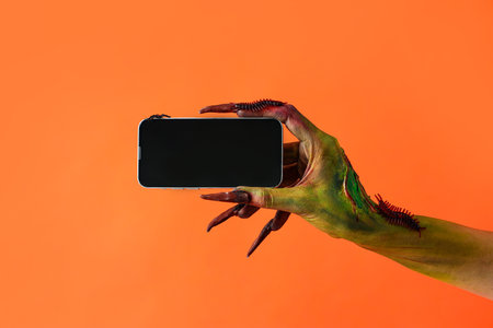 Witch with mobile phone on orange background. Halloween celebrationの写真素材