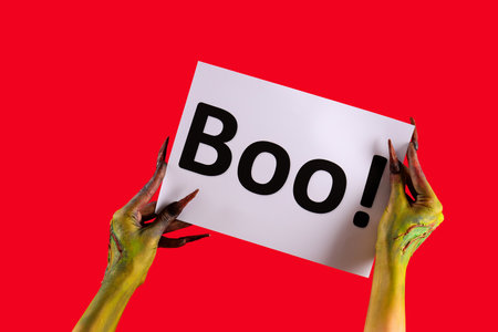 Witch holding paper with word BOO on red background. Halloween celebrationの写真素材
