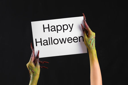 Witch holding paper with text HAPPY HALLOWEEN on black backgroundの写真素材