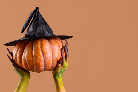 Witch holding pumpkin with hat on beige background. Halloween celebrationの写真素材