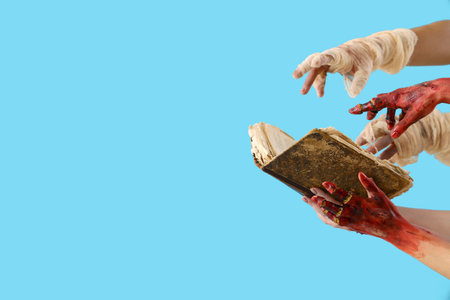 Zombie and mummy hands with ancient book on blue background. Halloween celebrationの写真素材