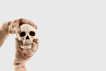 Mummy hands holding skull on white background. Halloween celebration