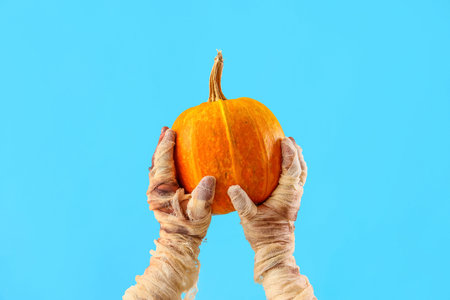 Mummy hands holding pumpkin on blue background. Halloween celebration