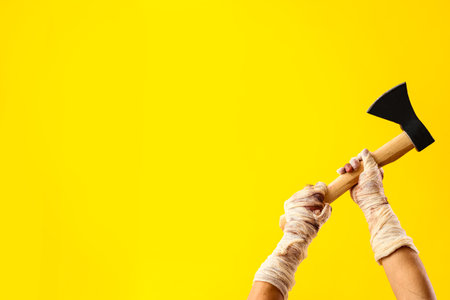 Mummy hands with ax on yellow background. Halloween celebrationの写真素材
