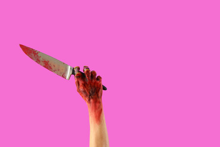 Zombie hand with bloodstained knife on pink background. Halloween celebration