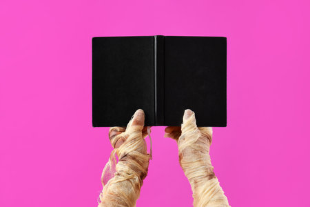Mummy hands with hardcover book on pink background. Halloween celebrationの写真素材