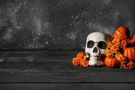 Halloween composition with skull, pumpkins and marigold flowers on black wooden tableの写真素材