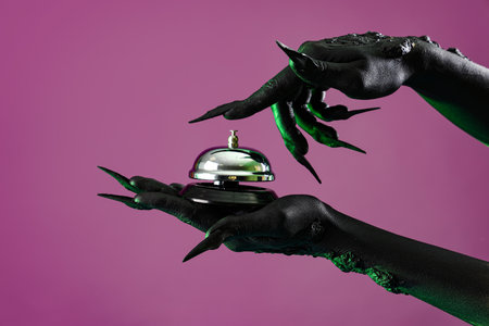 Green hands of witch with hotel bell on purple background. Halloween celebrationの写真素材