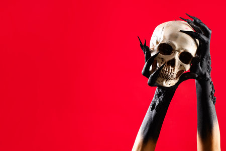 Black hands of witch with human skull on red background. Halloween celebrationの写真素材