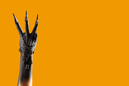 Black hand of witch with claws on orange background. Halloween celebration