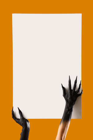Black hands of witch holding blank poster on orange background. Halloween celebrationの写真素材