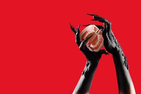 Black hands of witch with jaws on red background. Halloween celebration