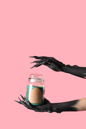 Black hands of witch holding jar with blank label on pink background. Halloween celebrationの写真素材
