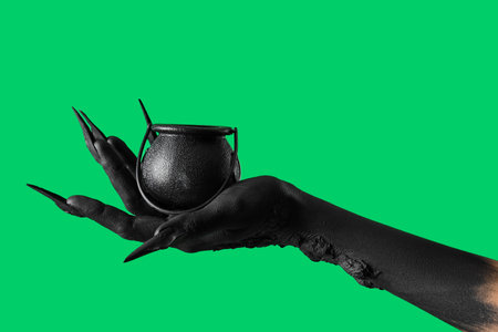 Black hand of witch with cauldron on green background. Halloween celebrationの写真素材