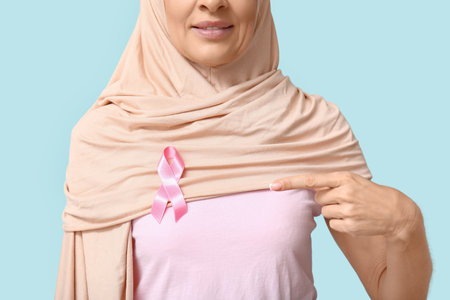 Muslim mature woman with pink ribbon on blue background, closeup. Breast cancer awareness conceptの写真素材