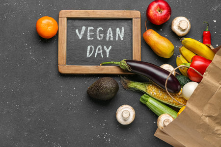Board with text VEGAN DAY, fresh vegetables and fruits on black backgroundの写真素材