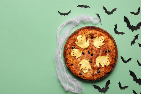 Wooden board with tasty pizza and paper bats for Halloween party on green backgroundの写真素材
