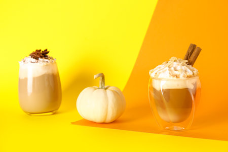 Glasses of tasty pumpkin latte with cinnamon, almond and star anise on colorful backgroundの写真素材