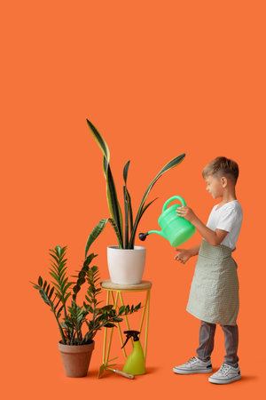 Cute little gardener watering plant on orange backgroundの写真素材