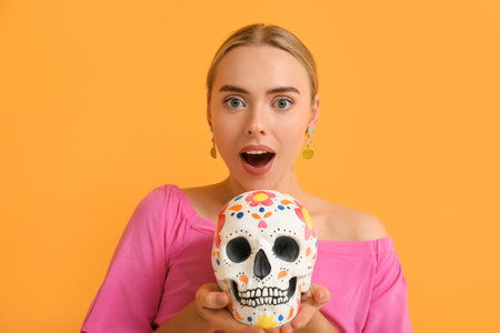 Pretty young woman with painted human skull on orange backgroundの写真素材