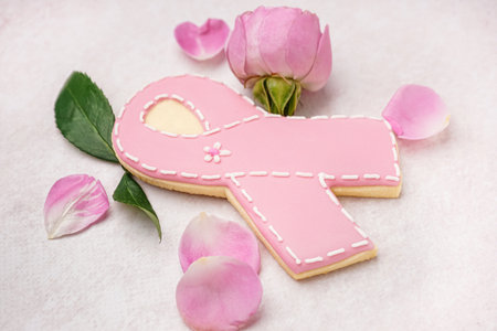 Pink cookie in shape of ribbon and rose flowers on gray grunge background. Breast cancer awareness conceptの写真素材