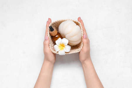 Woman holding basket with bottle of essential oil, bath sponge and flower on light background, closeupの写真素材