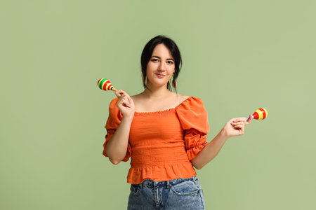 Beautiful happy woman with maracas on green background