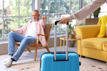 Mature woman with suitcase leaving her husband at home, closeup. Divorce conceptの写真素材