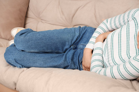 Young woman suffering from stomach ache on sofa at home, closeupの写真素材