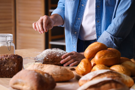 Young man with loaves of fresh bread at table in bakery