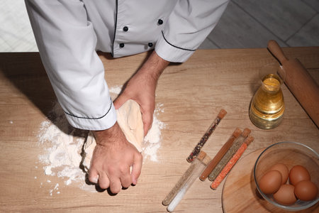 Young chef kneading dough on table in bakery