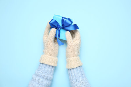 Female hands in warm mittens with Christmas gift on color background, closeupの写真素材