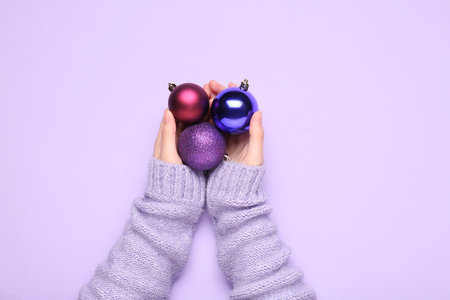 Female hands with beautiful Christmas balls on lilac background, closeupの写真素材