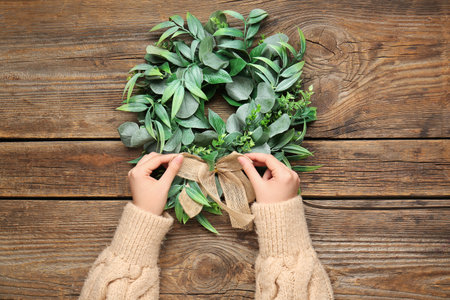 Female hands with stylish Christmas wreath on wooden background, closeupの写真素材