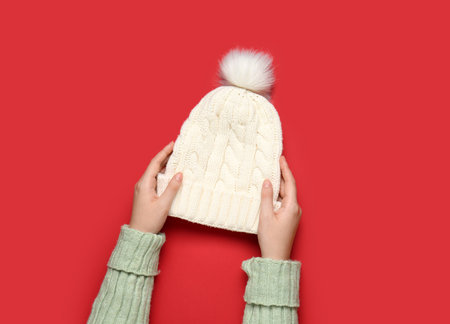Female hands with knitted warm hat on red background, closeupの写真素材