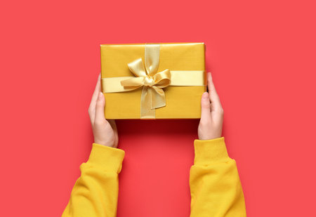 Female hands with Christmas gift on red background, closeupの写真素材