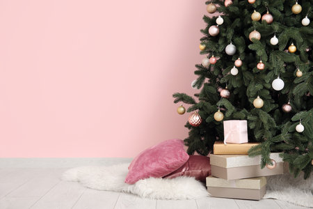 Christmas tree with baubles and gift boxes near pink wallの写真素材