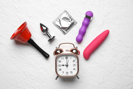 Alarm clock with different toys and condom on grunge white background. Time for sexの写真素材