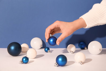 Female hands with Christmas balls on white table against blue backgroundの写真素材