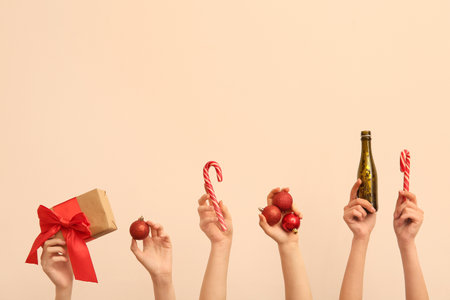 Female hands holding Christmas balls, bottle of champagne, candy canes and gift box on beige backgroundの写真素材