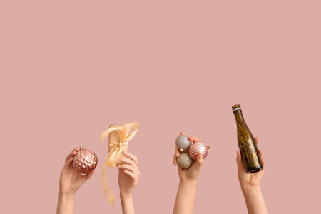 Female hands holding Christmas balls, bottle of champagne and gift box on pink backgroundの写真素材