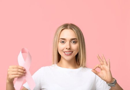Young woman with ribbon showing OK on pink background. Breast cancer awareness conceptの写真素材